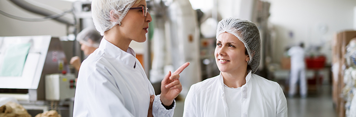 Two female workers discussing while standing in food factory.